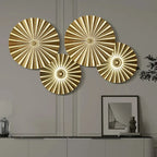 Set of four gold decorative wall plates on a neutral wall with a framed picture and lamp.