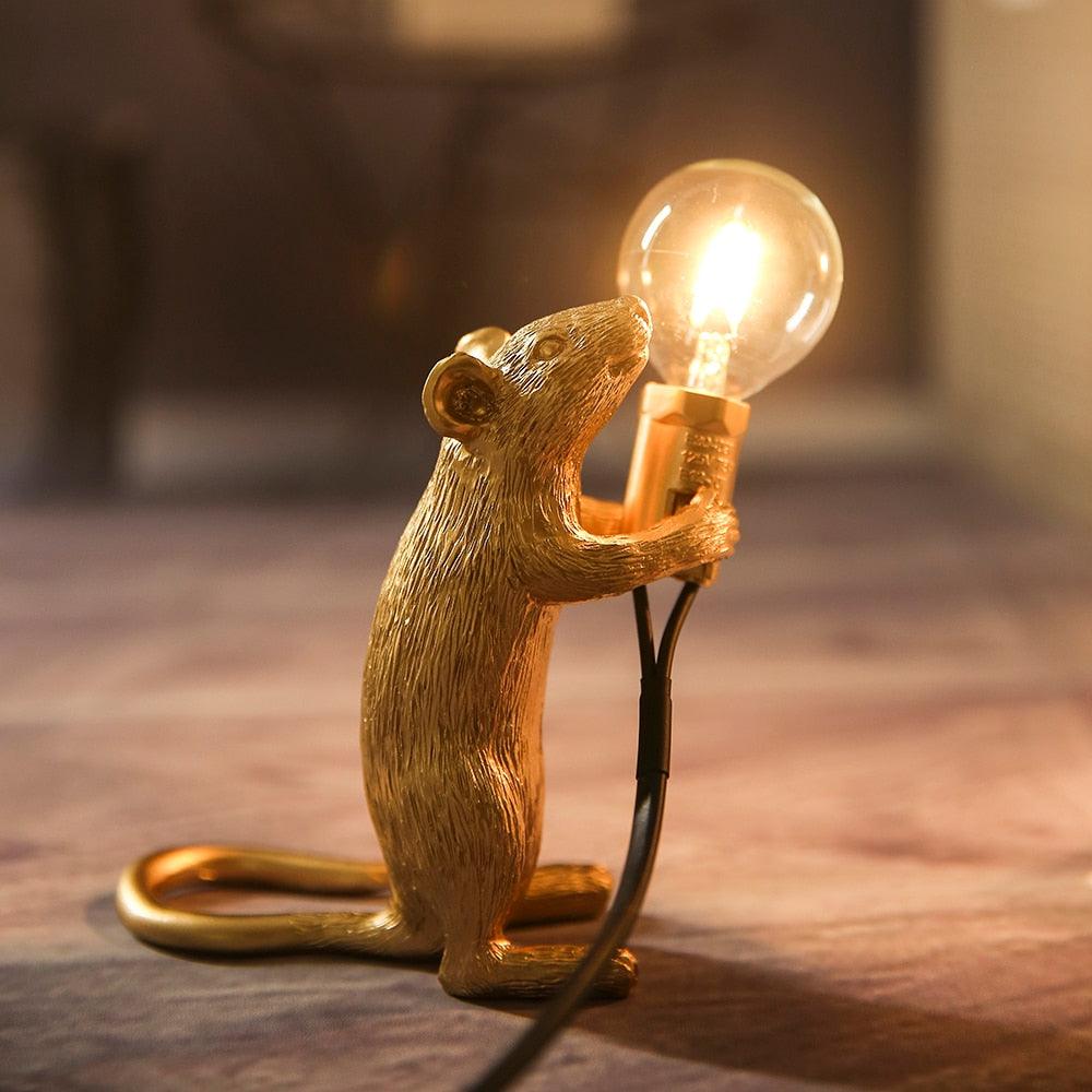 Gold mouse figurine holding a light bulb on a wooden surface