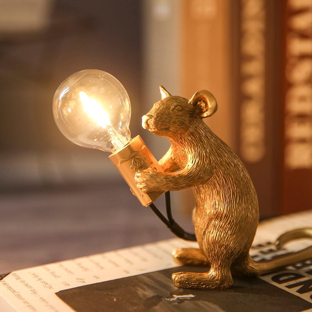 Gold mouse figurine holding a light bulb on a surface with a blurred background