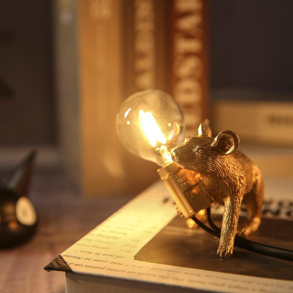 Gold bear figurine with a lit light bulb on top, placed on a surface with books in the background.