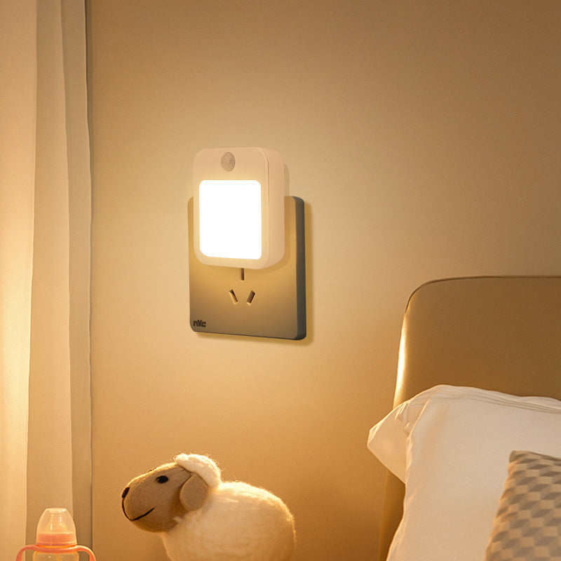Night light attached to a wall near a bed with a plush toy sheep in the foreground.