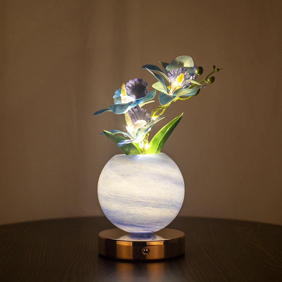 Decorative lamp with glowing flowers in a marble-like vase on a dark surface.