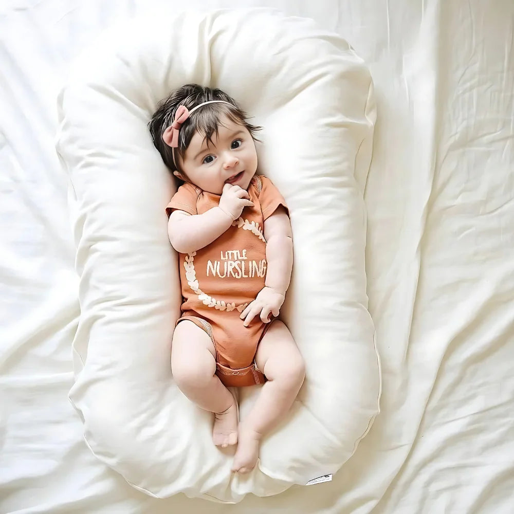 Baby in an orange 'Little Nursling' outfit lying on a white pillow