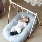 Baby lying on a light blue cushion with a wooden play gym in a room.