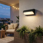 Outdoor wall light fixture on a wall with plants and a patio in the background