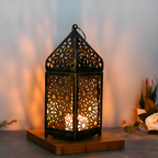 Decorative lantern with intricate patterns on a wooden base, emitting a warm glow against a blurred background.