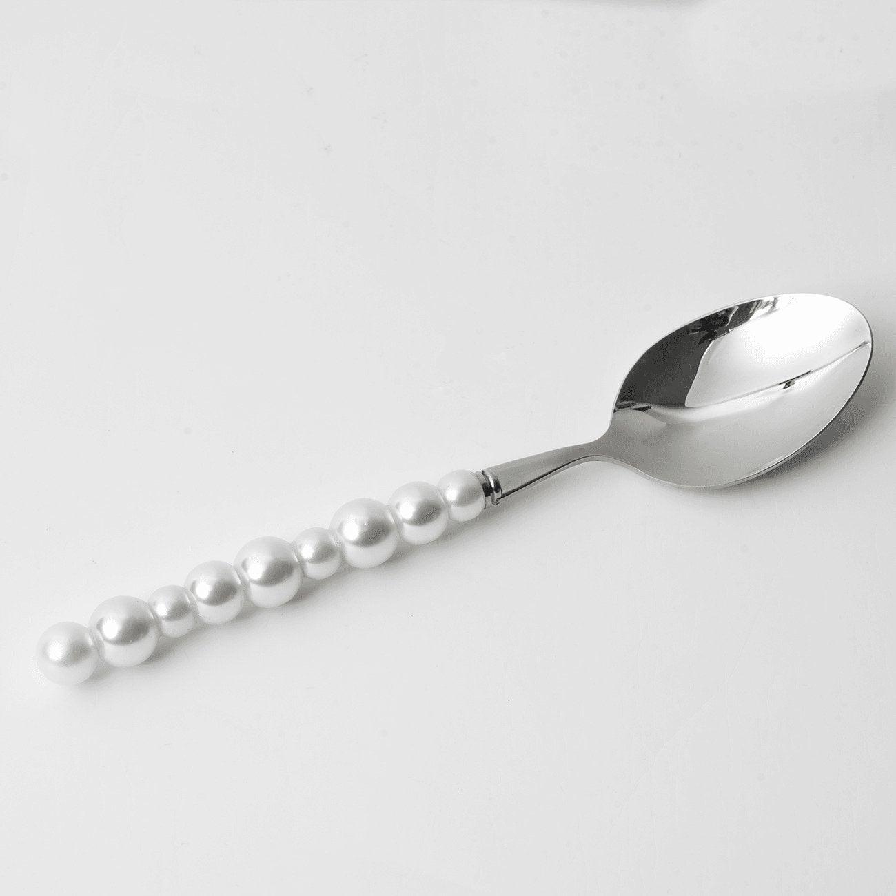 Silver spoon with pearl-like beads on a light gray background