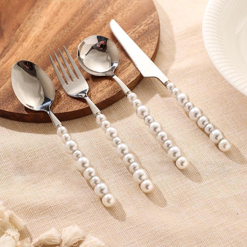 Silver cutlery set with pearl handles on a wooden board and beige surface.