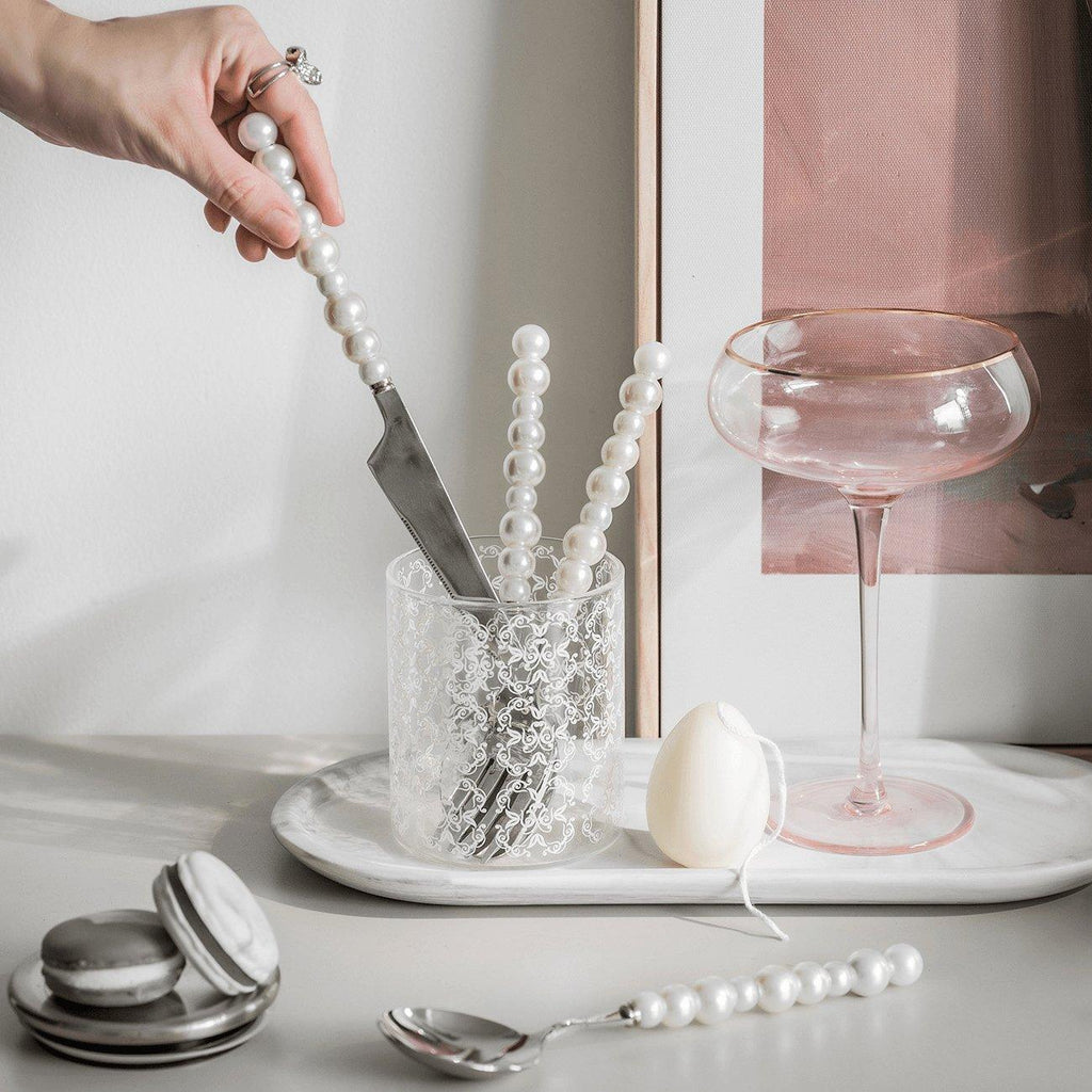 Person holding a knife with pearl handles over a glass container on a table with various items.