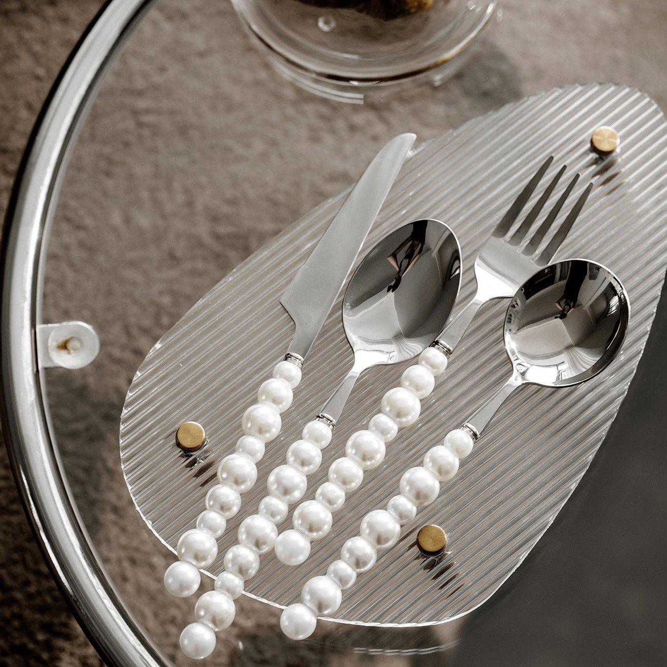 Silver cutlery set with pearls on a textured surface