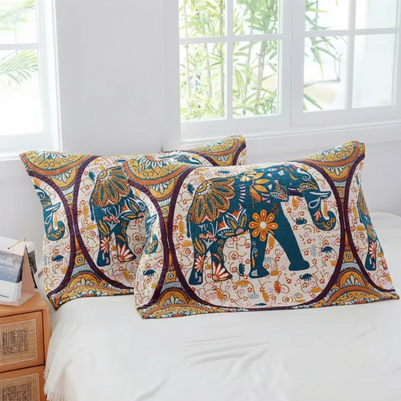 Two decorative rectangular throw pillows with an intricate elephant and floral mandala print, styled on a white bed in a bright bedroom setting.