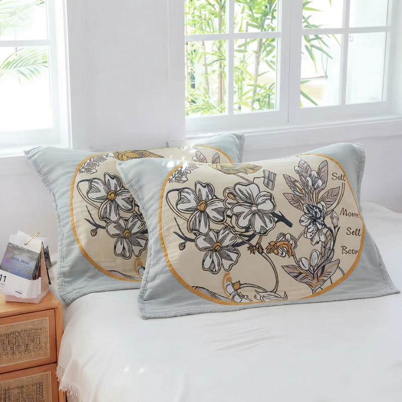 Two decorative rectangular throw pillows with a floral print and gold script text, resting on a white bed in a bright bedroom setting.