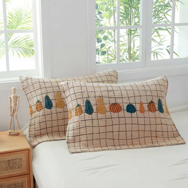 Two decorative pillowcases with a beige grid pattern and embroidered autumn pumpkins in orange, yellow, and teal, styled on a white bed in a bright bedroom.