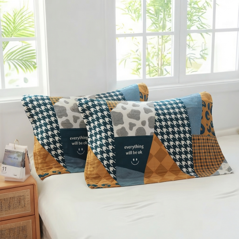 Two rectangular patchwork pillows with a 'everything will be ok' smiley face design, styled on a white bed in a bright bedroom setting.