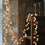 Warm white LED string lights draped over a rustic stone wall and wooden shelf in an indoor setting.