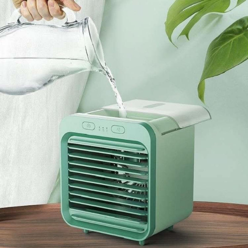 Person pouring water into a small green air cooler on a wooden surface with a light green background.