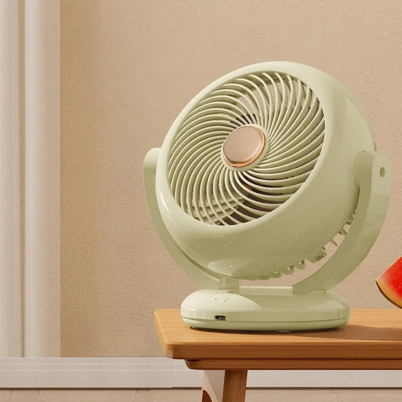 Green oscillating table fan on a wooden surface with a beige wall background
