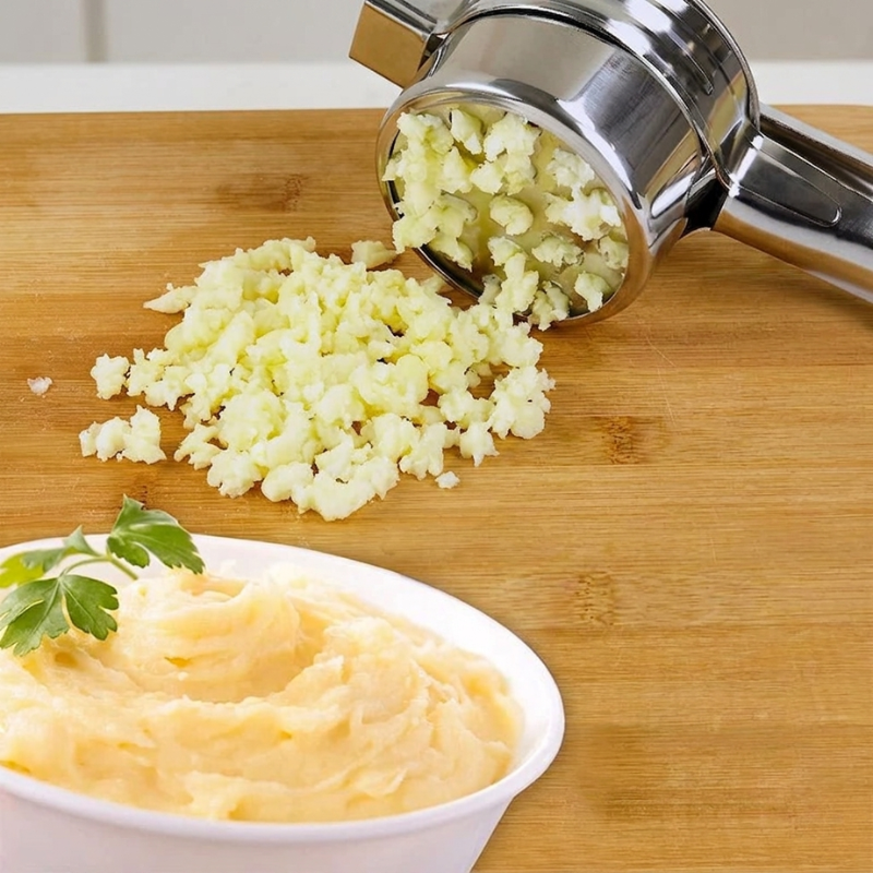 Mashed cauliflower on a wooden cutting board with a hand masher, next to a bowl of mashed cauliflower.
