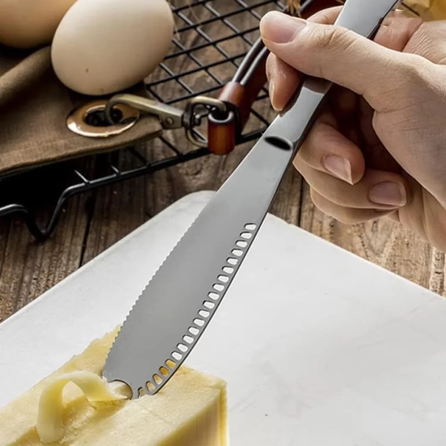 Hand using a butter knife to spread butter on bread with eggs and a pan in the background.