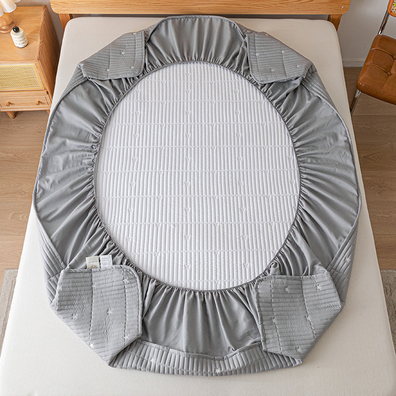 Gray crib sheet on a crib with a wooden side table in the background