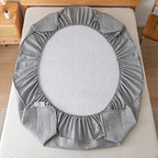 Gray crib sheet on a crib with a wooden side table in the background