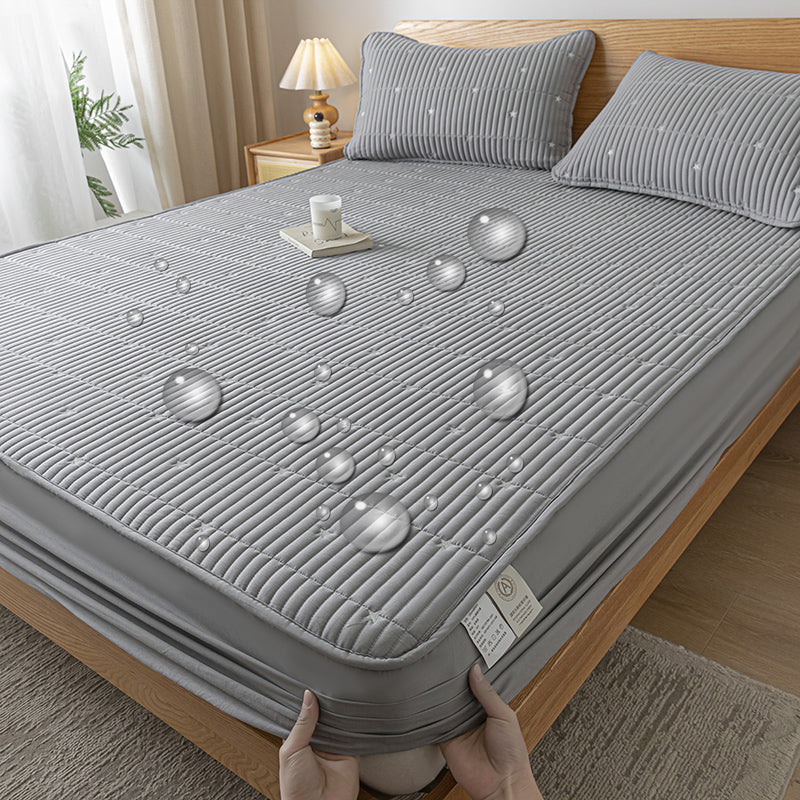 Gray textured mattress cover being held on a bed in a bedroom setting.