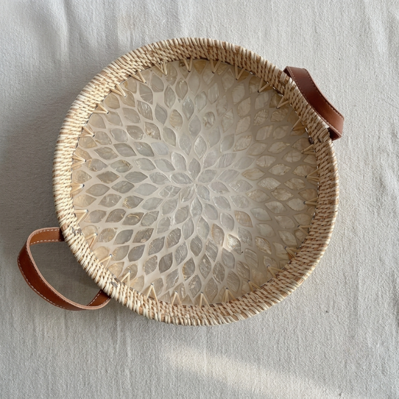 Round woven basket with a floral pattern and brown leather handles on a light gray background