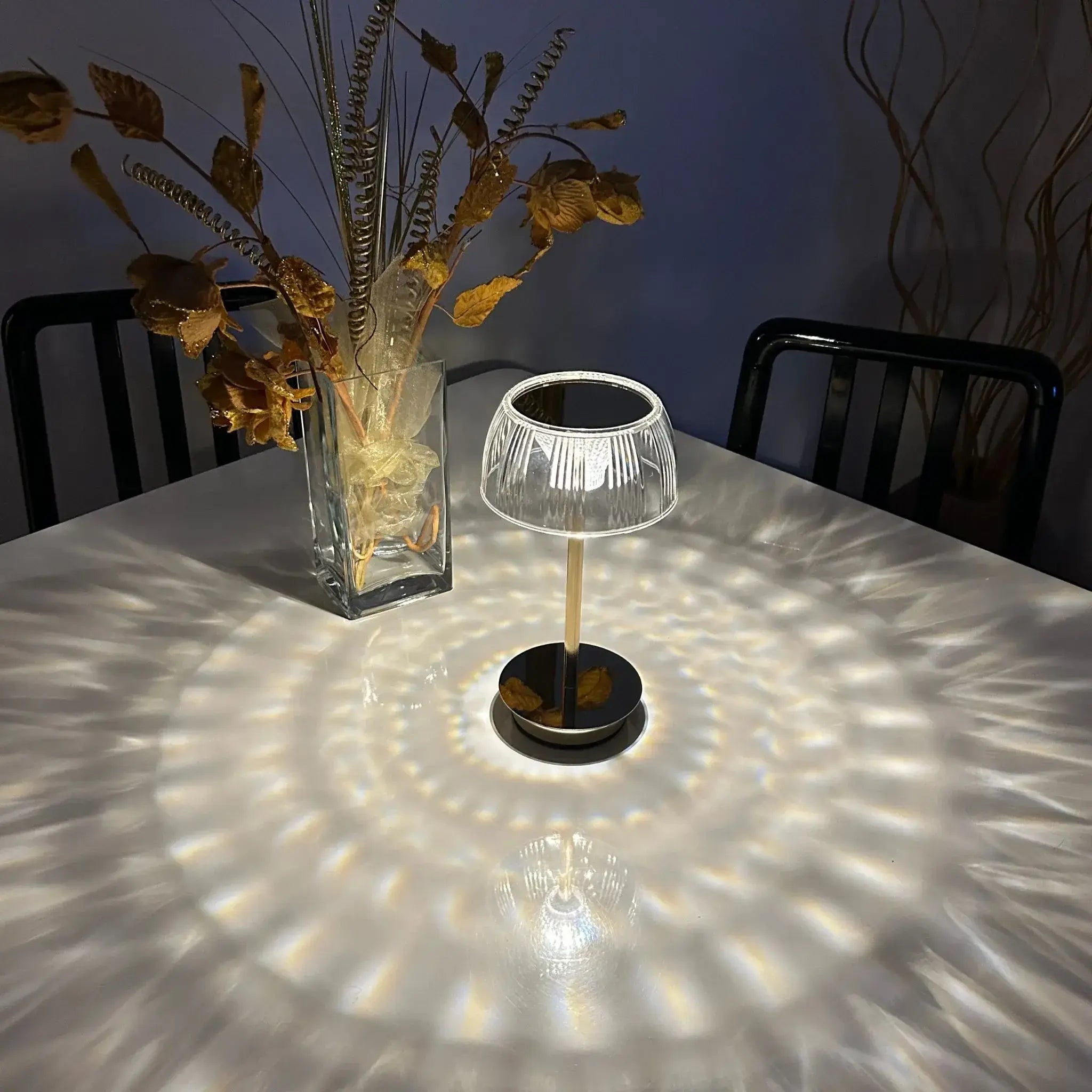 Small table lamp casting a pattern on a table with a vase of dried plants in the background.