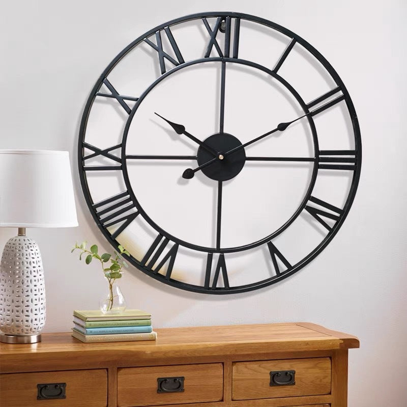 Large black wall clock with Roman numerals on a white wall above a wooden cabinet.