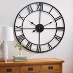 Large black wall clock with Roman numerals on a white wall above a wooden cabinet.