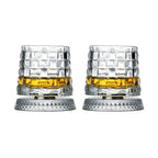 Two crystal glasses with diamond pattern filled with amber liquid on a white background