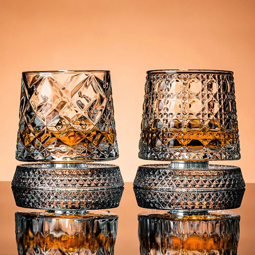 Two crystal glasses filled with a amber liquid on a reflective surface with a peach-colored background.