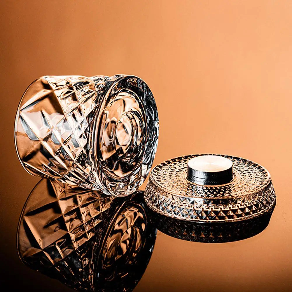Decorative glass container with intricate design on a reflective surface against an orange background