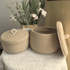 Two woven baskets with lids on a textured surface with a plant in the background.