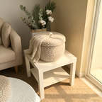 White side table with woven basket and plant in a cozy living room.
