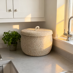 Woven storage basket on a kitchen counter with a plant and window in the background