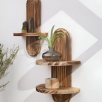 Three rustic wooden floating shelves with arched backing plates, styled with home decor items including a glass vase with green stems and a candle, mounted on a white wall.
