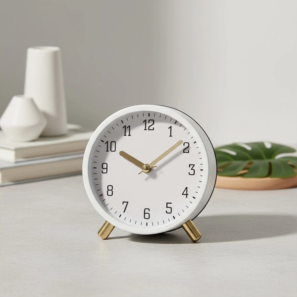 White clock with gold hands on a light surface, with decorative items in the background.
