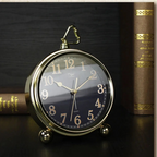 Vintage-style clock with gold frame and black face on a dark surface with books in the background