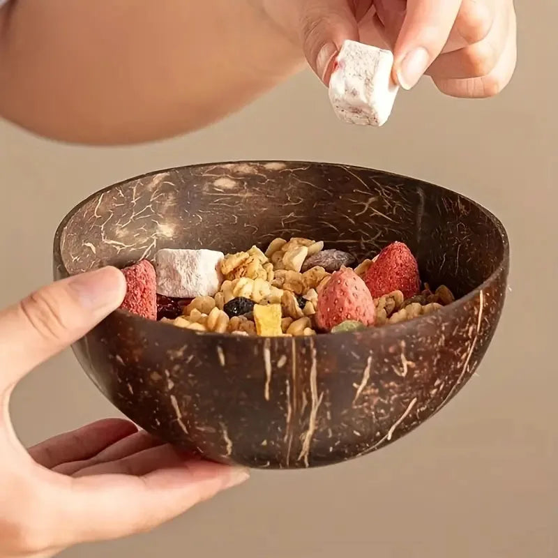 Coconut shell bowl with granola and strawberries, held by a person against a neutral background