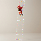 A tall LED light ladder with a small Santa Claus figurine climbing it, photographed against a plain light gray studio background.