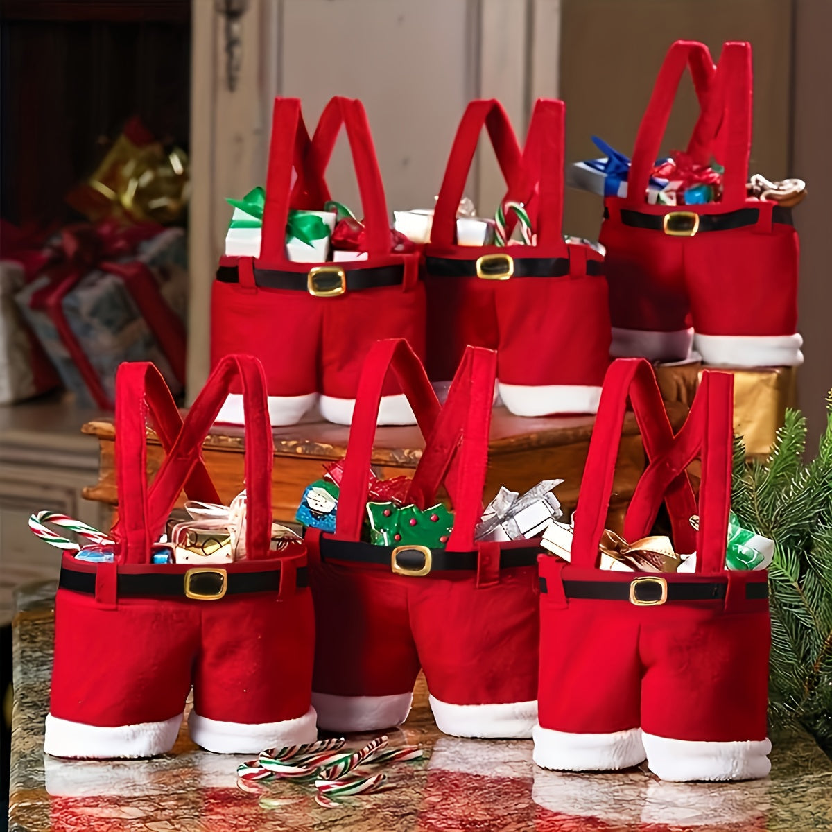 Red Santa pants with suspenders filled with candy on a table.