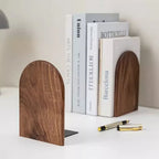 Wooden arch-shaped bookends with books and pens on a white surface