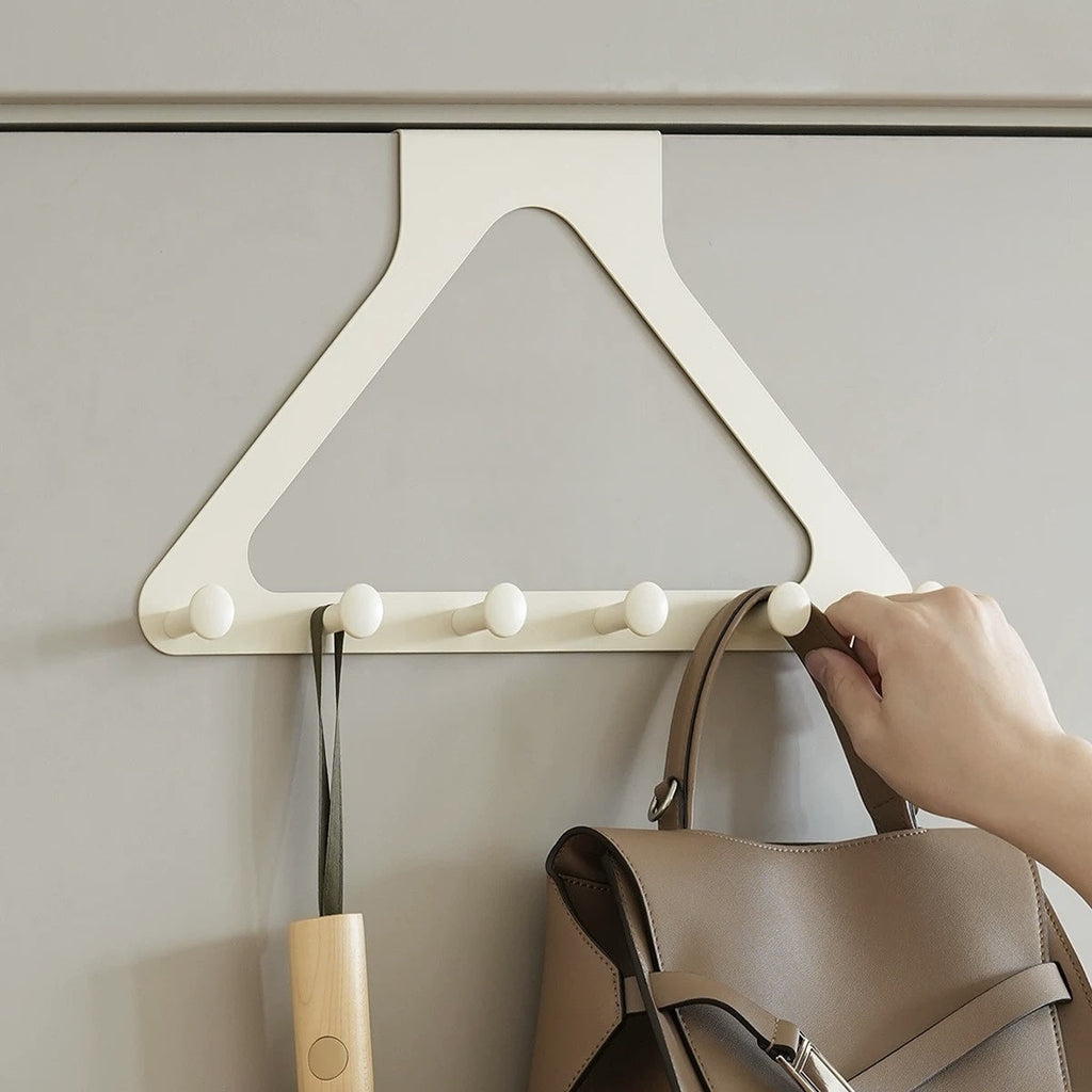 Wooden coat rack with hooks on a gray wall, with a hand placing a bag on one of the hooks.