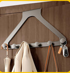 A modern wall-mounted triangular coat rack with five round hooks, shown attached to a brown wooden door. A cream coat hangs from one hook, and keys and straps are attached to the right side.