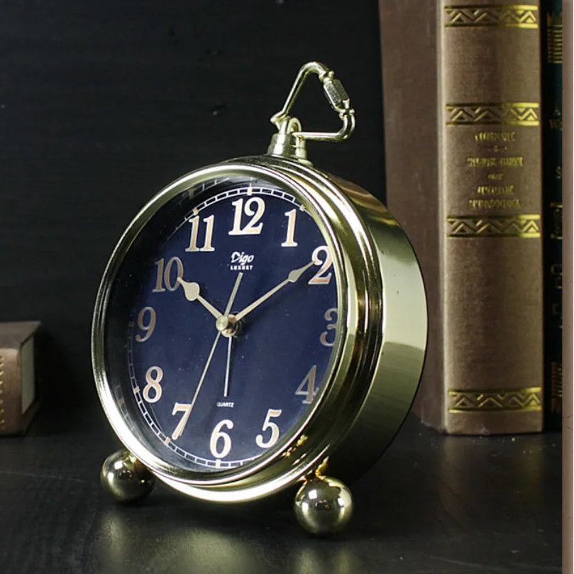 Vintage-style clock with blue face and gold casing on a dark surface with books in the background
