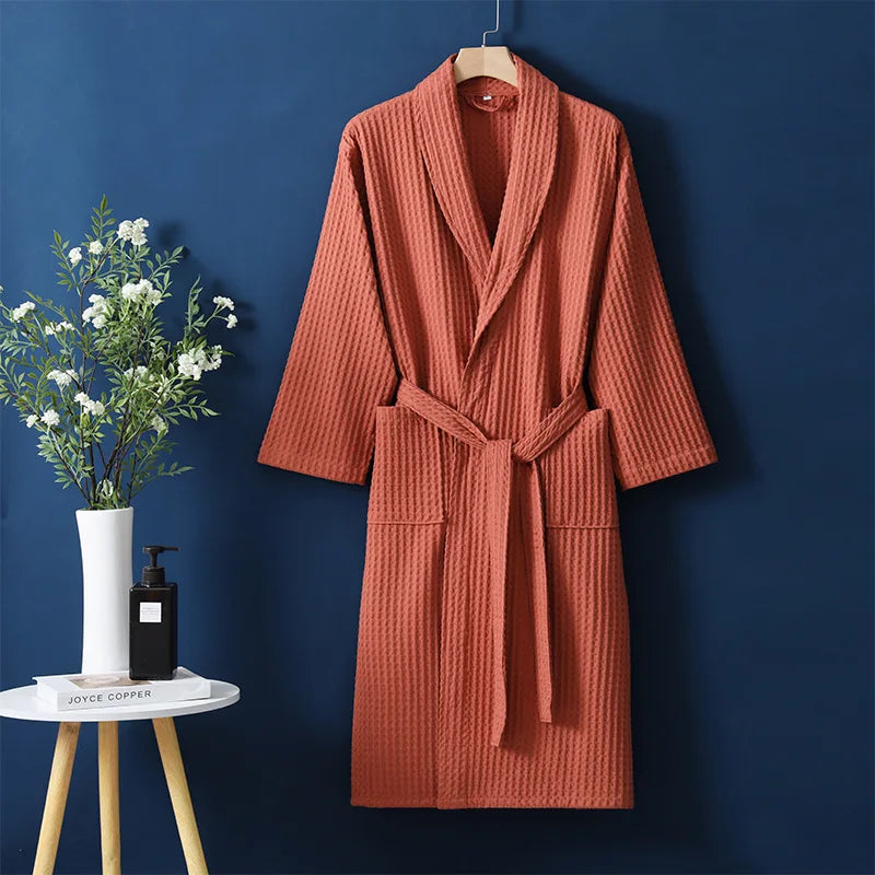 Orange robe hanging on a hanger against a blue wall with a small table and plant in the foreground.