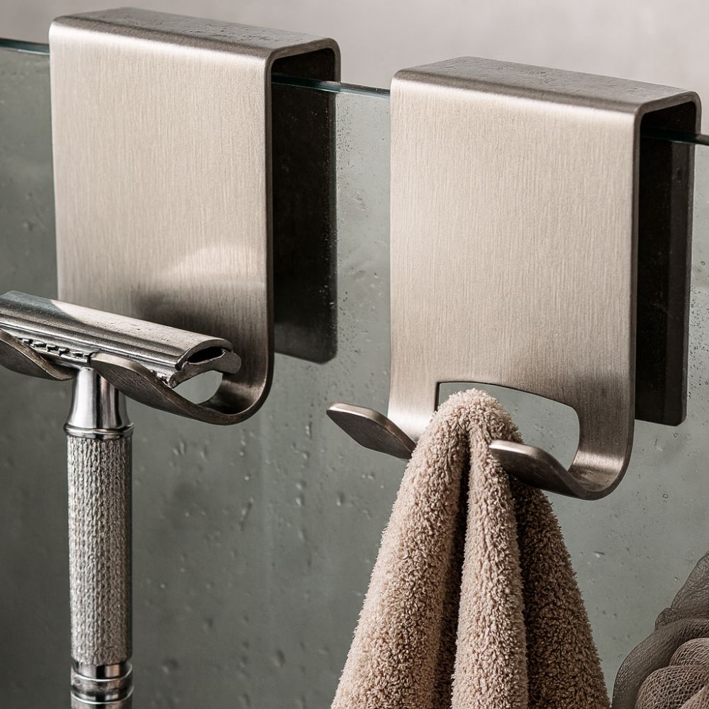 Metallic wall hooks with a towel and razor on a glass surface