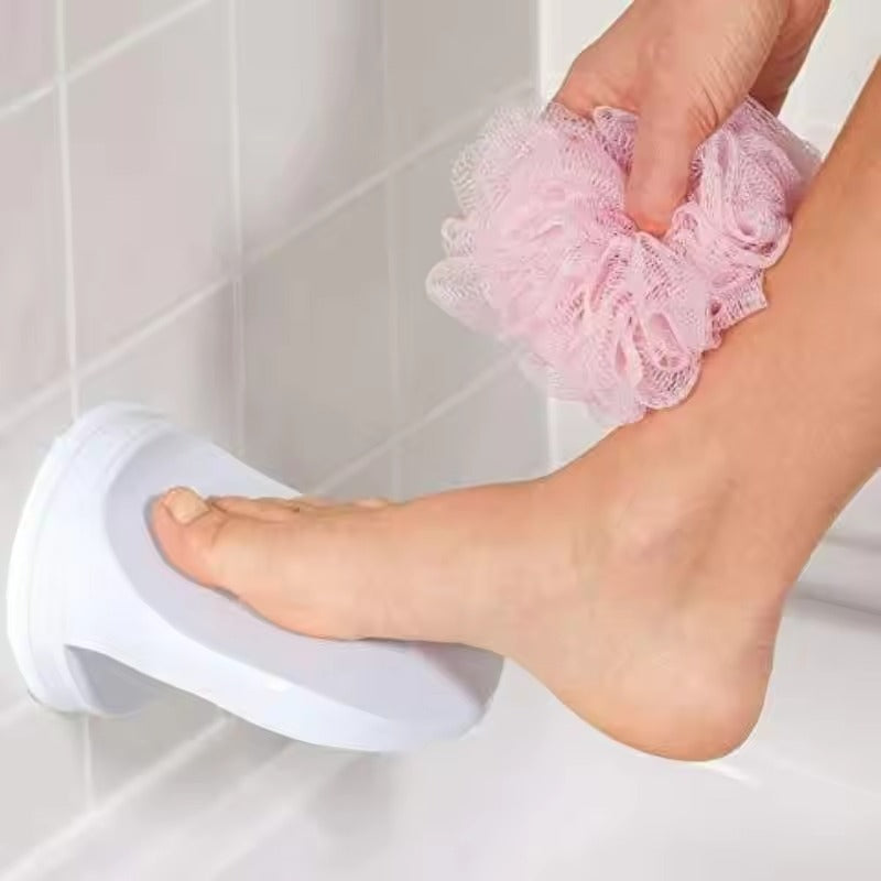 Person using a pink loofah on their foot next to a white stool in a tiled bathroom.