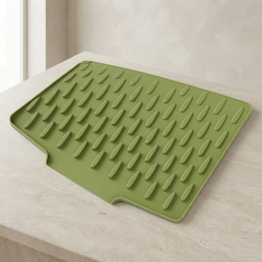 An olive green silicone dish drying mat with raised drip edges, shown resting on a light beige stone countertop against a matching tiled wall.
